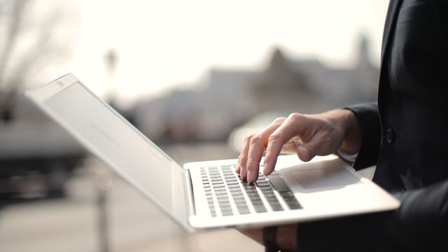 A business professional typing on a laptop in an outdoor setting, symbolizing remote work.